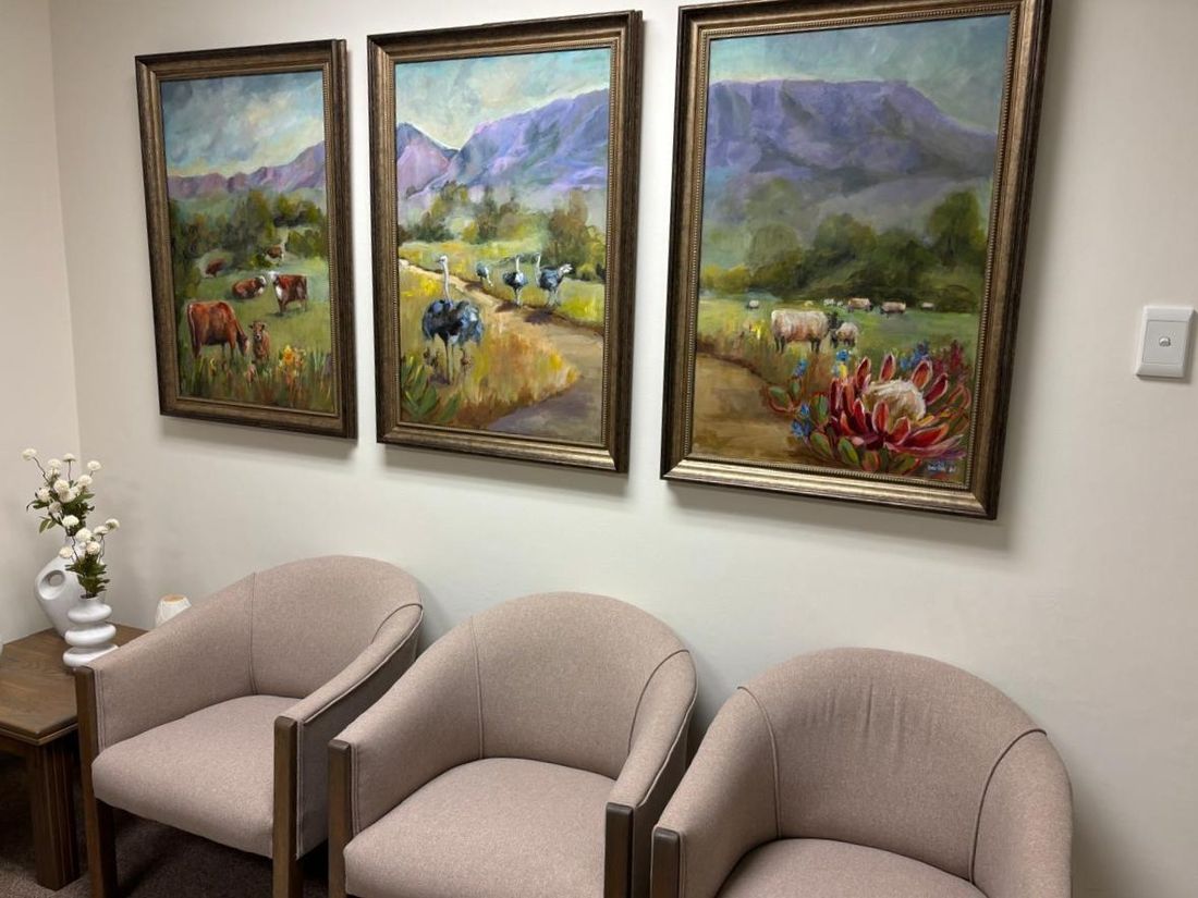 Three framed landscape paintings of cattle, ostriches and sheep hung together above a row of chairs